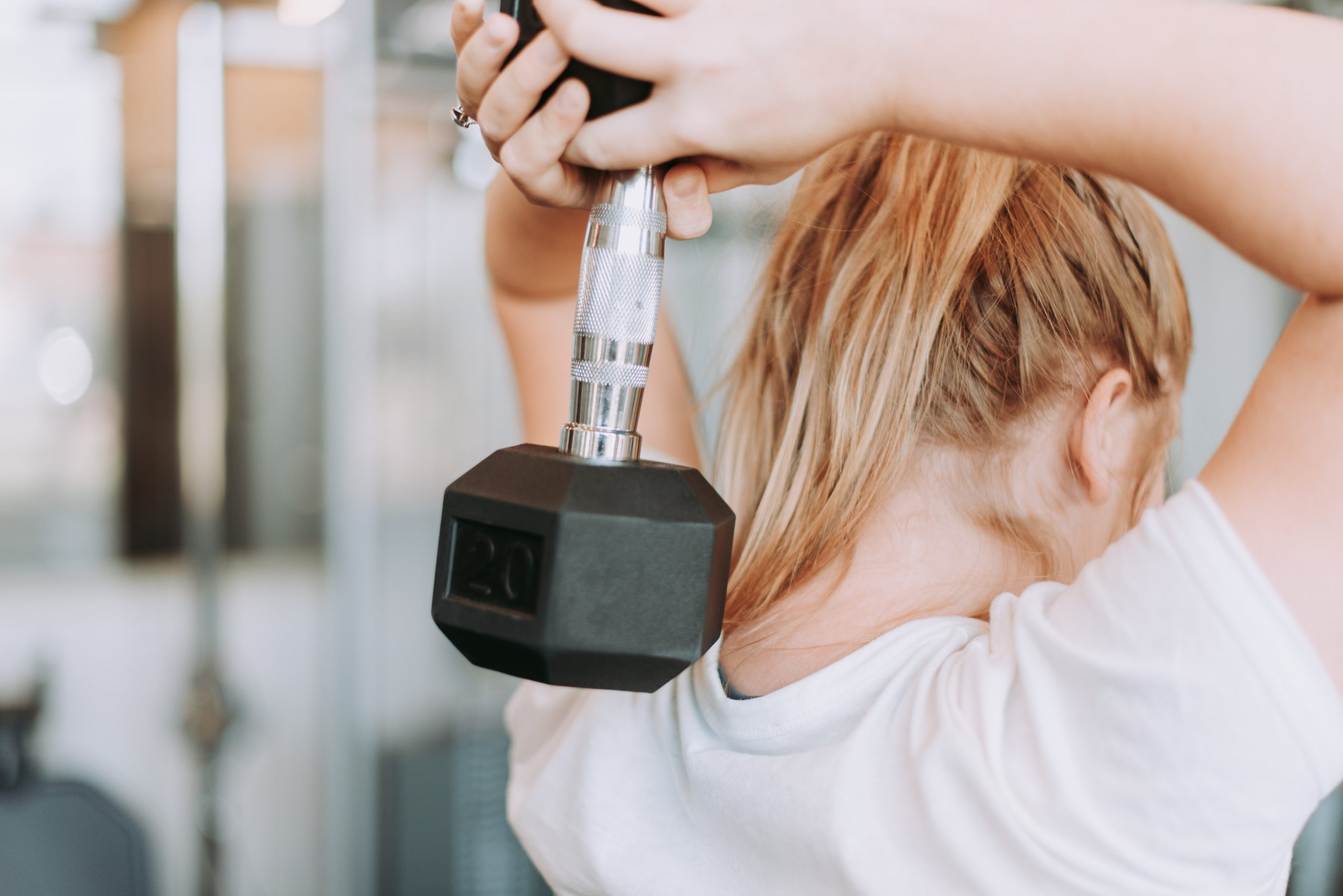 A woman works out at home with dumbbell and instruction from online coach Everfit
